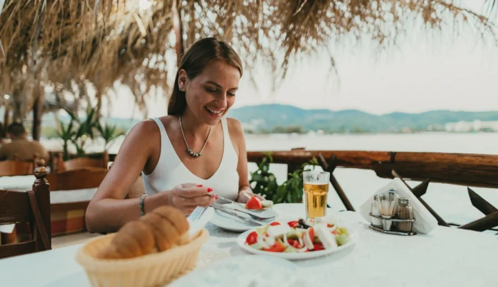 Personalized experiences: How retailing software meets hospitality's growing demand - Woman sits at hotel restaurant patio enjoying a beer and a salad with a smile - Sabre Hospitality