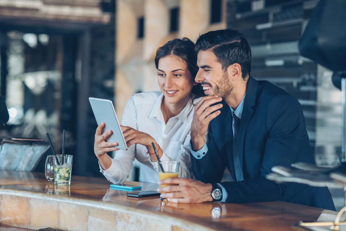 Hospitality software trends shaping the industry in 2025 - A man and a woman look at a device while enjoying drinks at a hotel - Sabre Hospitality