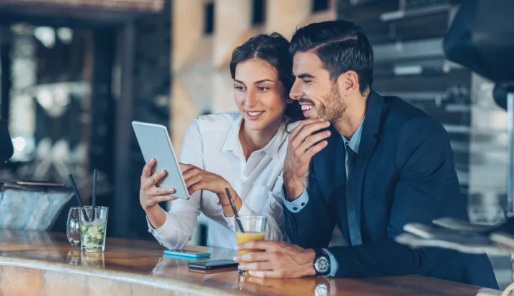 Unlock new revenue streams by merchandising hotel spaces - A man and a woman look at a tablet while enjoying drinks at a hotel bar - Sabre Hospitality