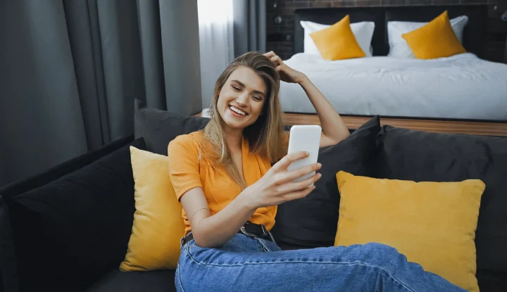 Email marketing for hotels: How to boost bookings and engagement. A woman sits on a hotel couch, smiling while looking at her phone