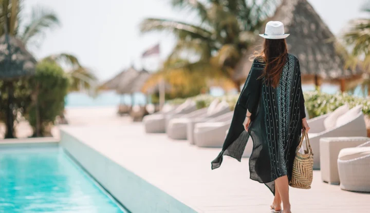 The role of hospitality software in enhancing guest satisfaction - A woman walks beside a pool at a beachfront hotel resort with a bag - Sabre Hospitality