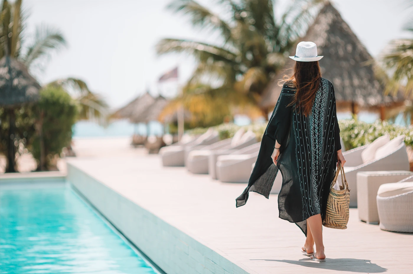 The role of hospitality software in enhancing guest satisfaction - A woman walks beside a pool at a beachfront hotel resort with a bag - Sabre Hospitality